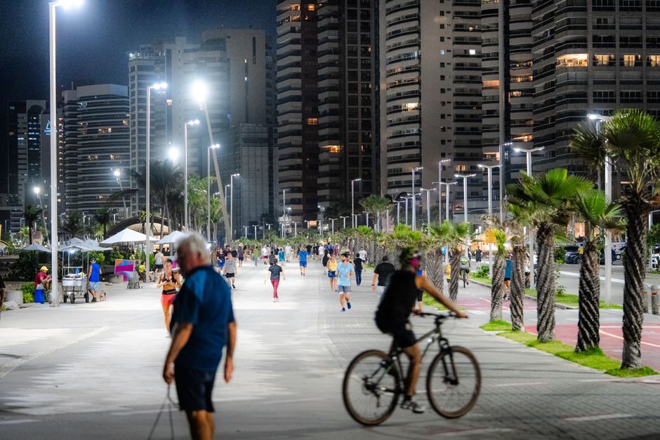 Homens e mulheres aproveitando a área de lazer urbana à noite, com destaque para atividades físicas e convivência em um ambiente contemporâneo na cidade.