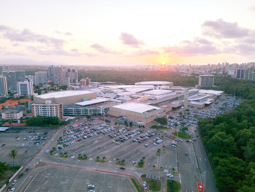 Visão aérea de um centro de convenções ou grande evento na cidade ao entardecer, com destaque para a enorme estrutura e estacionamento lotado.