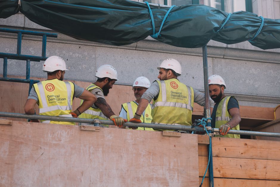 Homens trabalhando em uma construção civil em um ambiente de obra, usando capacetes e coletes de segurança, simbolizando o setor de construção e engenharia.