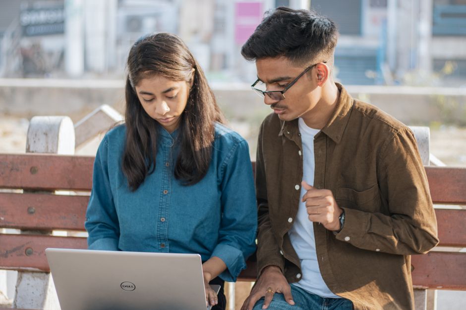 Juventudes discutindo ideias e trabalhando juntas ao ar livre com um laptop em um ambiente urbano.
