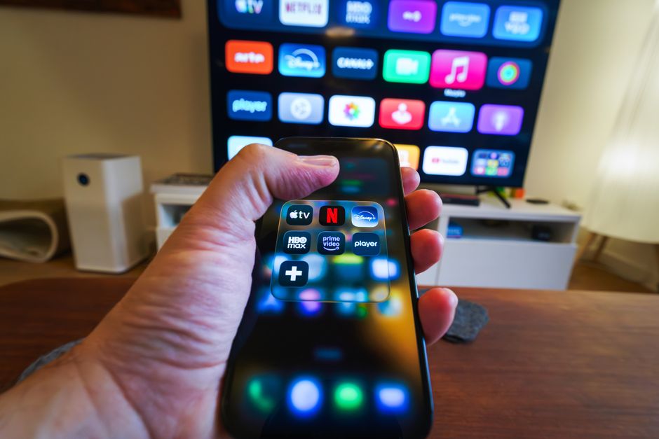 Pessoa controlando e acessando serviços de streaming em um smartphone, destacando o uso de tecnologia para entretenimento em casa.