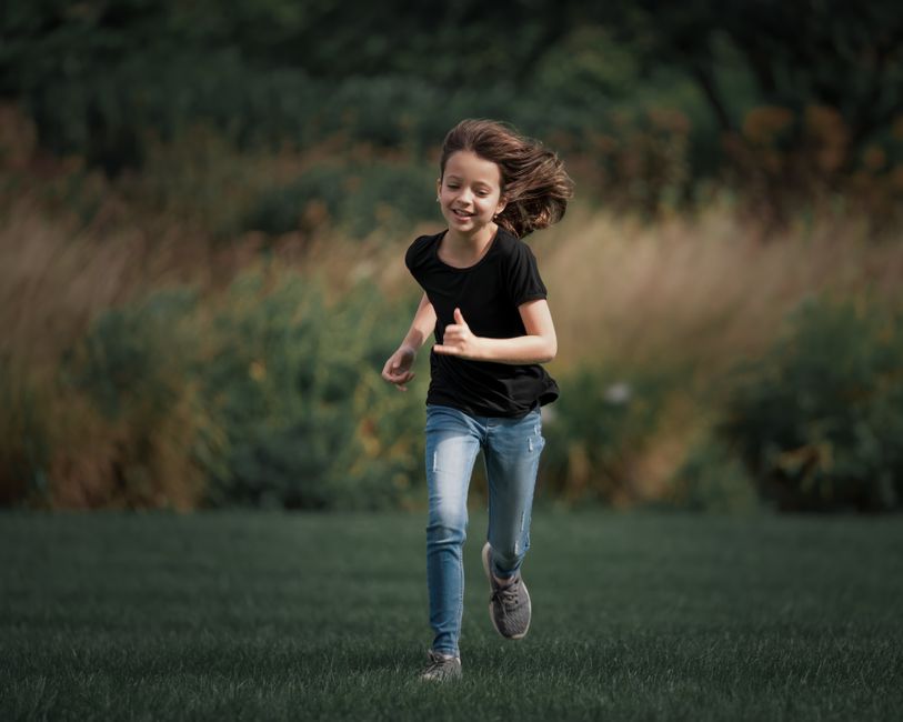 Menina feliz correndo ao ar livre em um ambiente natural, representando liberdade e bem-estar infantil.