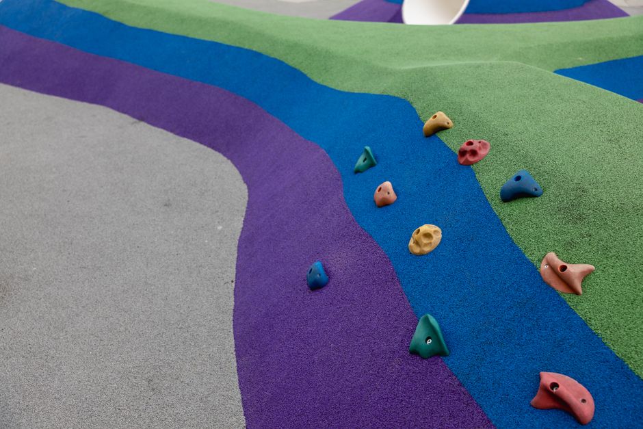 imagem de um espaço de lazer ao ar livre com paredes de escalada usando cores vibrantes como roxo, verde e azul, decoradas com agarras de escalada coloridas