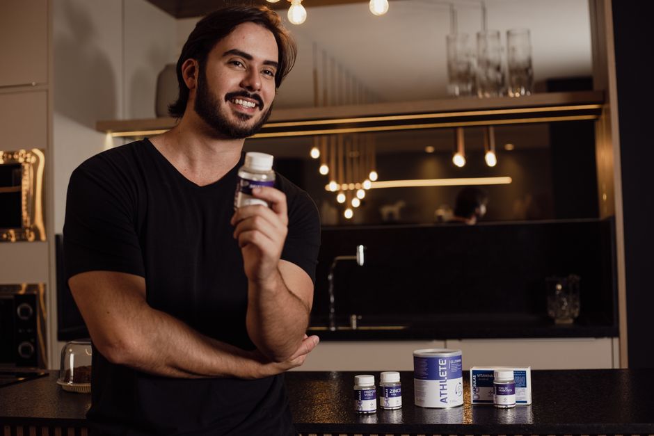 Homem sorrindo segurando um suplemento vitamínico em ambiente moderno, promovendo saúde e bem-estar.
