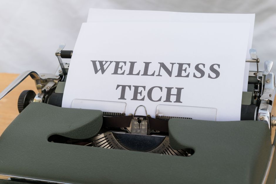 Imagem de uma máquina de escrever antiga com uma folha de papel que possui a frase 'WELLNESS TECH', ilustrando o tema de tecnologia e bem-estar.
