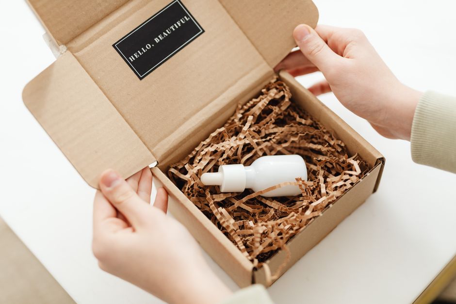 Imagem de uma pessoa abrindo uma caixa de papel marrom com um pequeno frasco de solução porta gota dentro, reconhecendo o tema de cuidados pessoais ou produtos de beleza para blog.