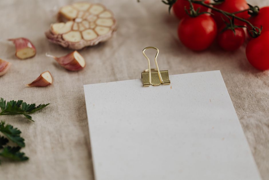 Imagem de uma mesa com ingredientes naturais ao fundo e uma folha de papel em branco presa por um clipe, ideal para um blog sobre culinária, ingredientes naturais ou receitas caseiras.
