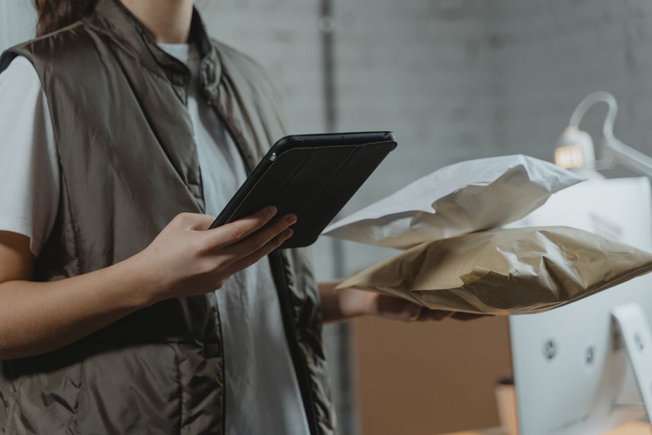 Pessoa utilizando um tablet na área de entrega ou logística, simbolizando o gerenciamento de pedidos e transporte.