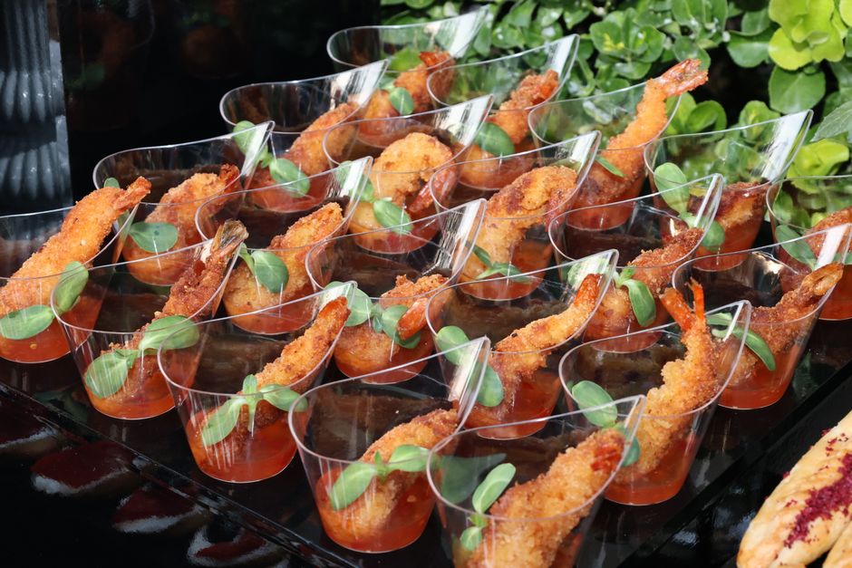 Imagem de aperitivos sofisticados de camarão empanado e molho, decorados com folhas verdes, servidos em copinhos transparentes