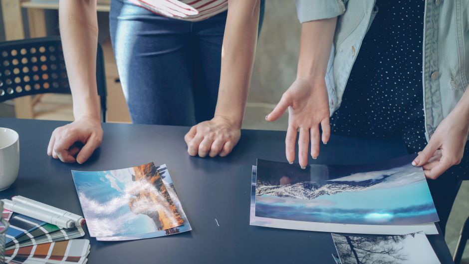 Duas pessoas analisando e discutindo fotos de paisagens naturais em um ambiente de trabalho colaborativo.