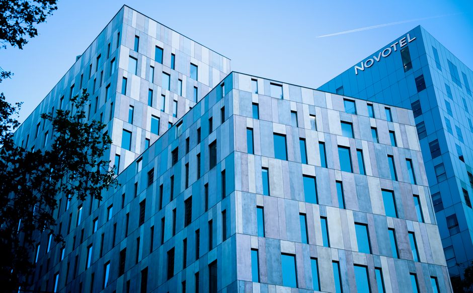 Imagem de um edifício moderno de escritórios com a marca Novotel, simbolizando negócios e gestão hoteleira.
