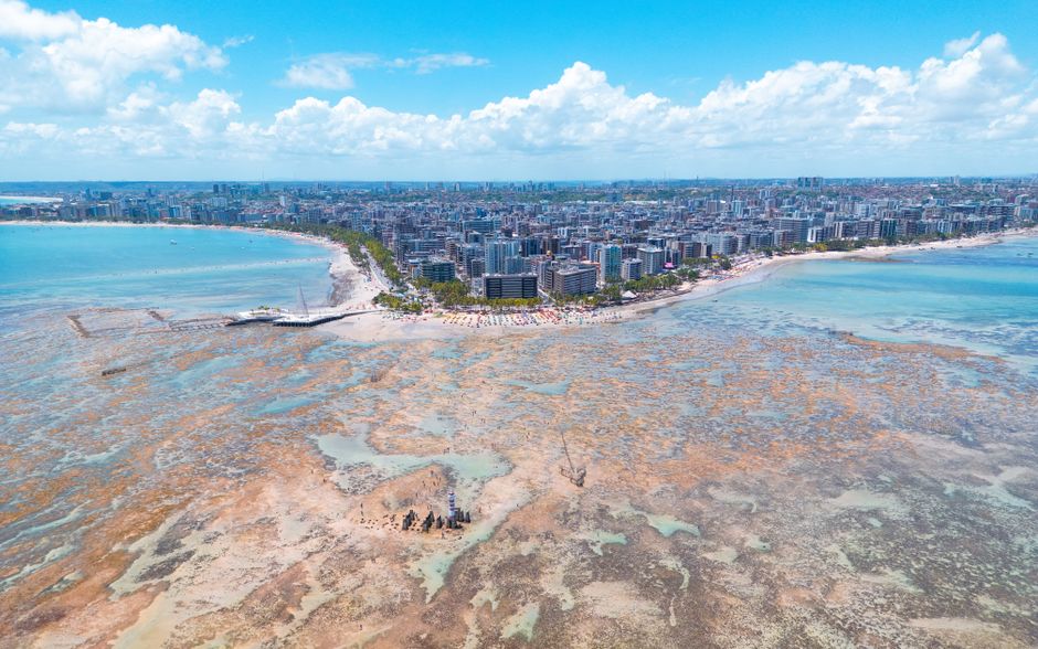 Vista aérea de uma área costeira urbana com expansão imobiliária e áreas de preservação ambiental na orla de uma cidade.
