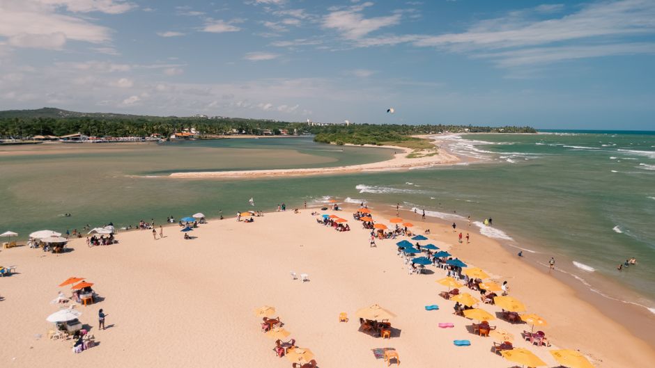 Praia movimentada com muitos banhistas, guarda-sóis coloridos e o mar ao fundo, representando lazer e turismo costeiro.