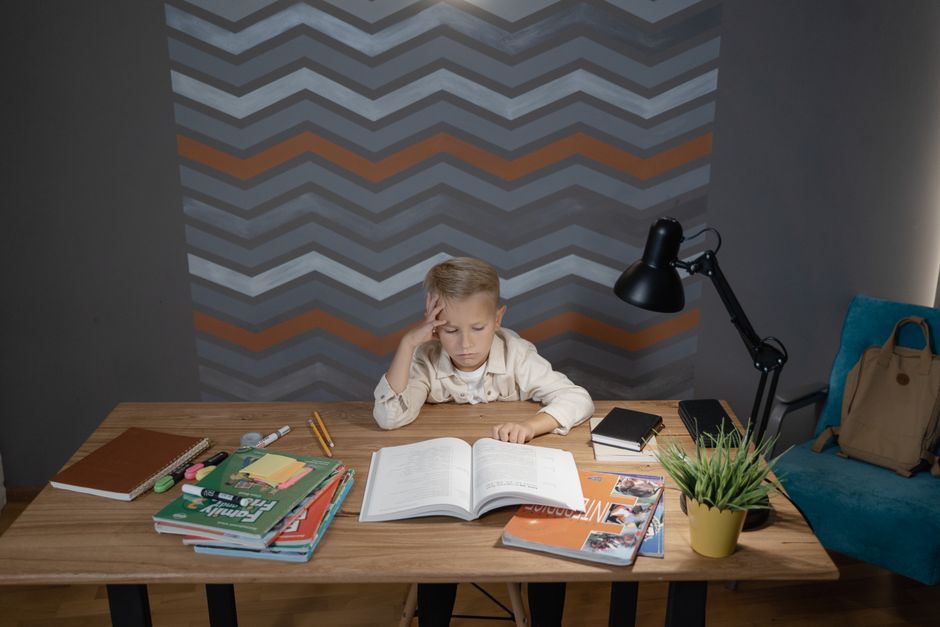 Criança estudando concentrada em uma mesa com livros, caderno e materiais escolares, em um ambiente de estudo ou sala de aula moderna.