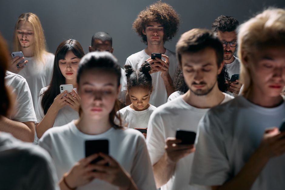 Grupo de jovens usando smartphones em um ambiente escuro, refletindo o impacto da tecnologia na juventude contemporânea.