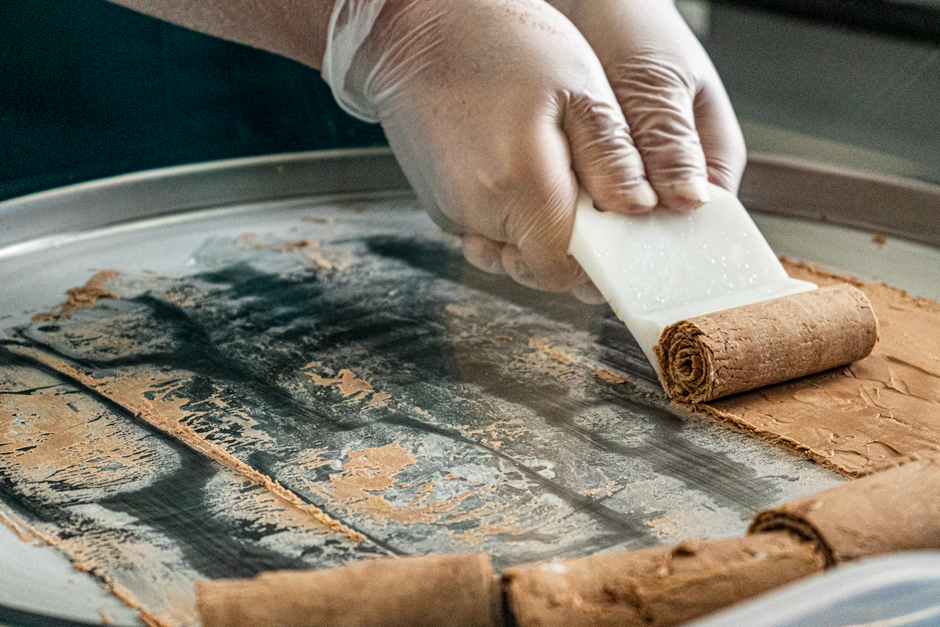 Pessoa preparando saboroso sorvete artesanal usando uma lâmina para moldar a massa em um equipamento especializado.