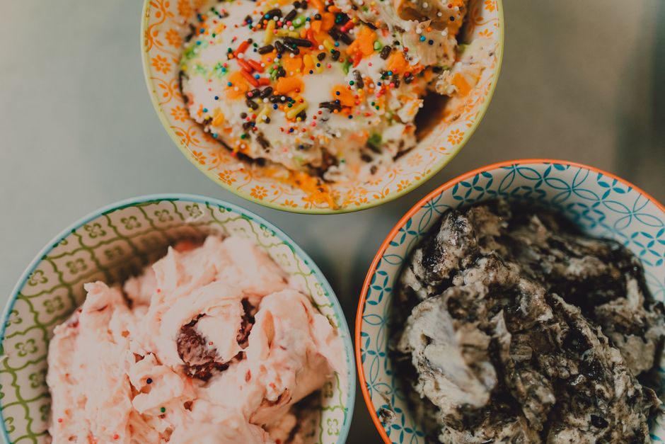 Três potes de sorvete diferentes, cada um com sabor e cobertura variados, apresentados em tigelas decoradas coloridas.