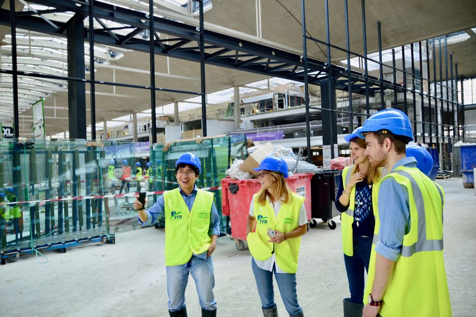 Grupo de profissionais em uma visita técnica a uma obra de construção civil, vestindo equipamentos de segurança e realizando inspeção no local.