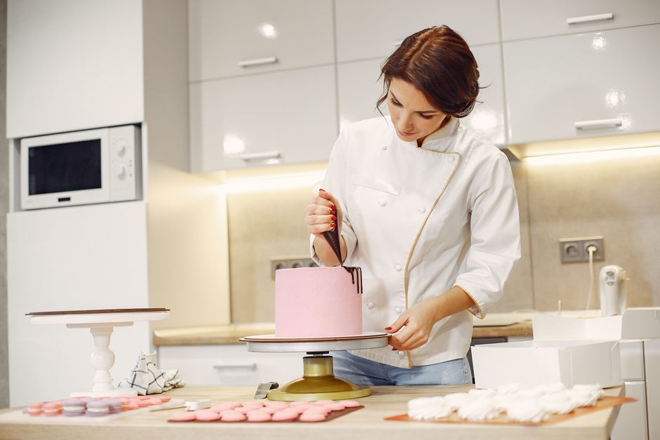 Mulher decoradora decorando um bolo em uma cozinha moderna, focada em confeitaria e artesanato gastronômico.
