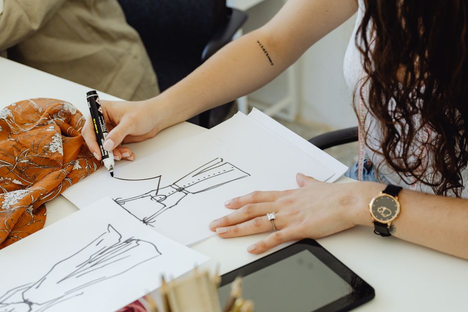 Mulher desenhando ideias criativas em um caderno, em um ambiente de trabalho colaborativo.