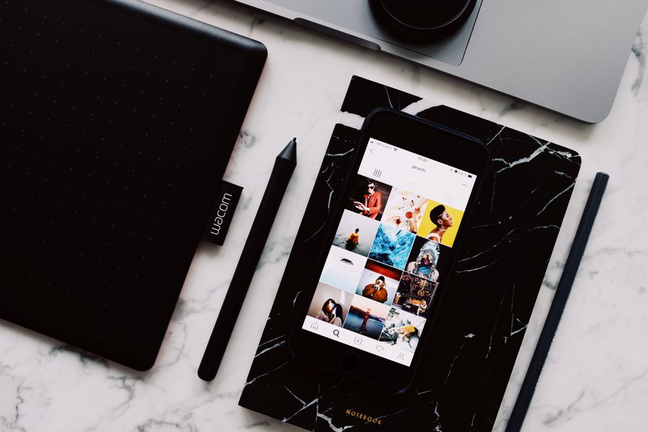 Imagem de uma mesa de trabalho com smartphone exibindo uma galeria de fotos, acompanhado de materiais de escrita e um laptop, sugerindo organização e criatividade no ambiente digital.