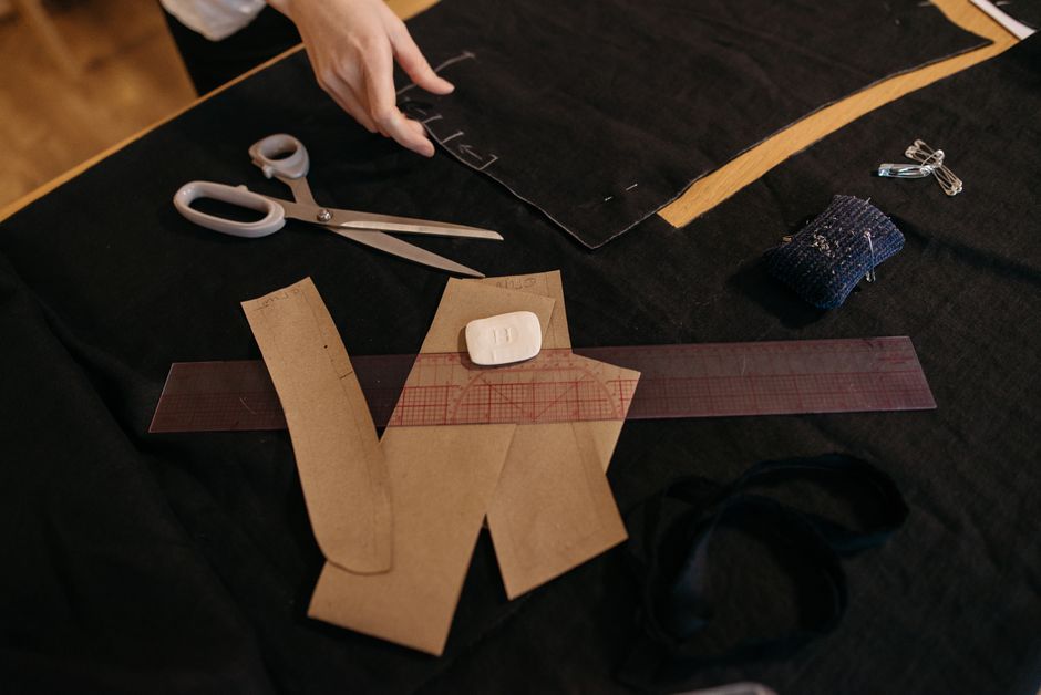 Imagem de uma mesa de trabalho com materiais de costura e molde de tecido, sugerindo criação de roupas ou confecção artesanal.
