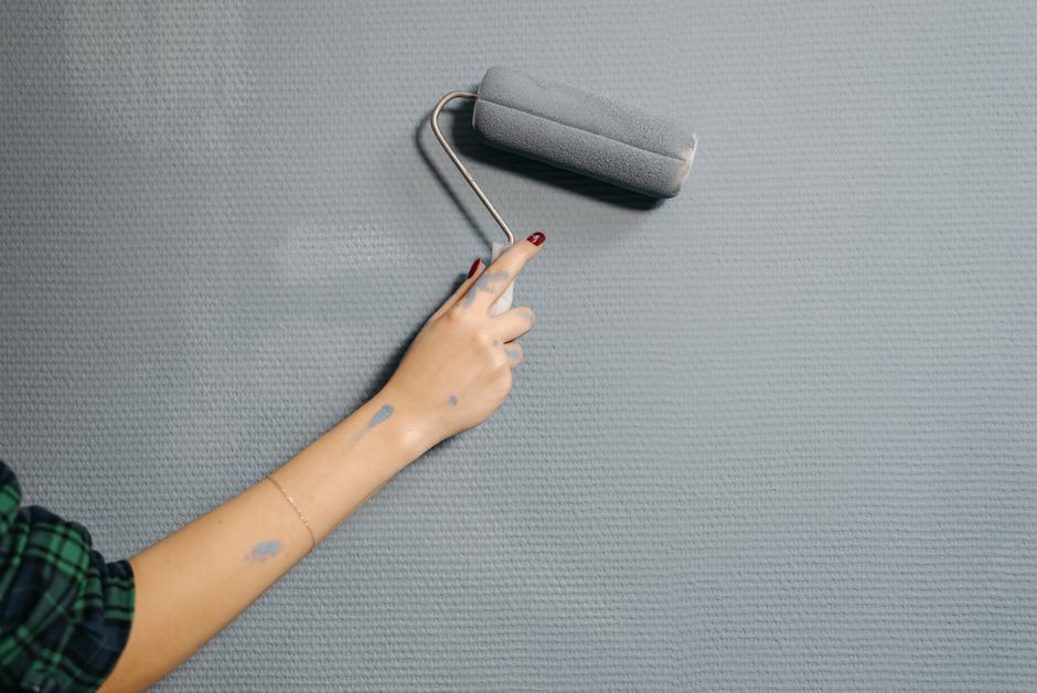 Mão pintando uma parede com rolo de tinta, simbolizando renovação e transformação no ambiente interno.