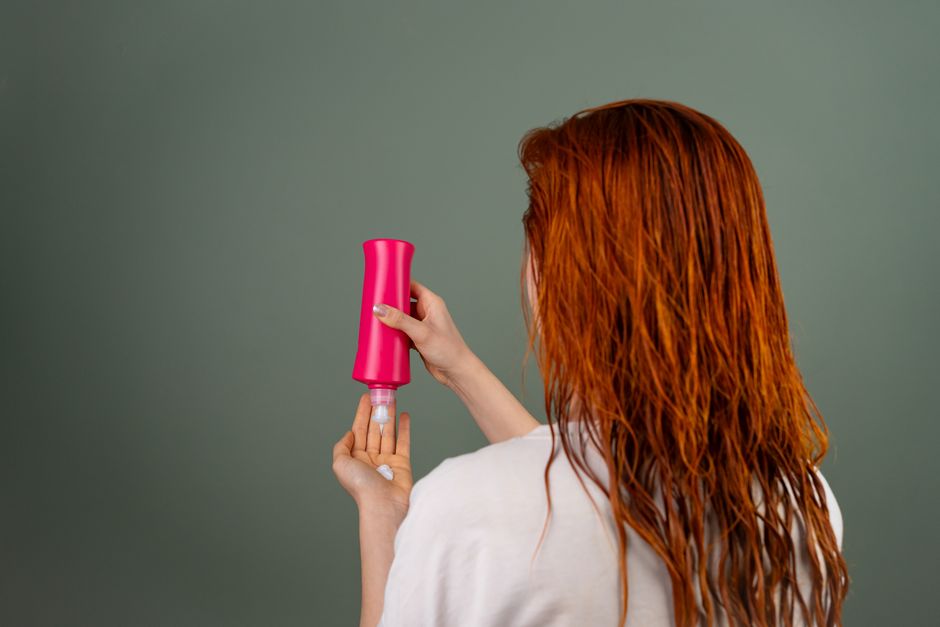 Mulher secando os cabelos com um secador de cabelo, destacando cuidados pessoais e beleza.