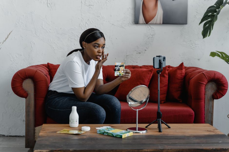 Mulher gravando um tutorial de beleza ou maquiagem em um ambiente interno, com foco nos procedimentos de cuidados pessoais.