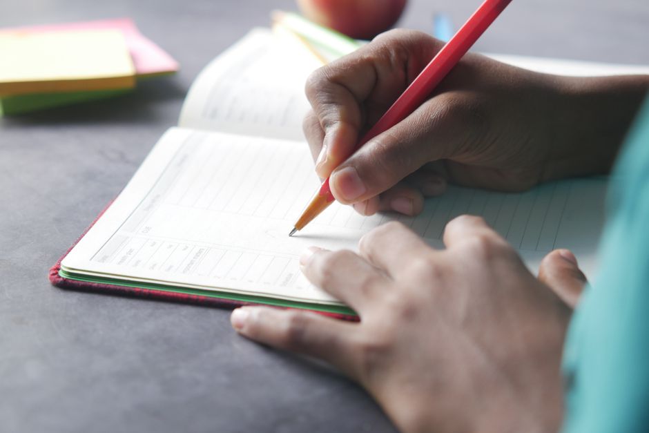 Pessoa escrevendo em um planner ou caderno, simbolizando organização e planejamento pessoal ou profissional.