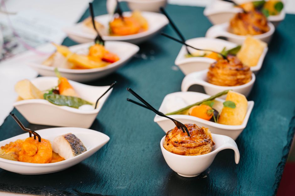 Variedade de mini porções sofisticadas de comida servidas em pequenas tigelas brancas, dispostas em uma mesa de festa ou evento gourmet.