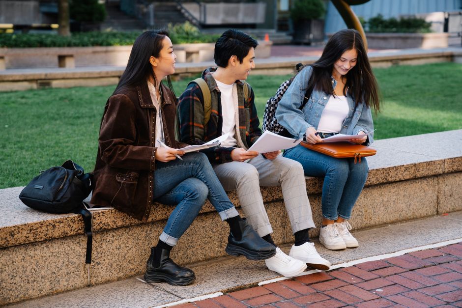 Grupo de estudantes sorridentes conversando e compartilhando materiais em um ambiente ao ar livre, simbolizando aprendizagem e convivência estudantil.