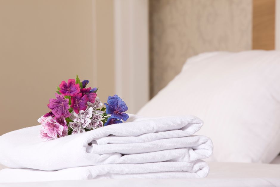Toalhas de banho dobradas com flores artificiais sobre uma cama, transmitindo aconchego e cuidado em ambiente de hospedagem ou pousada.