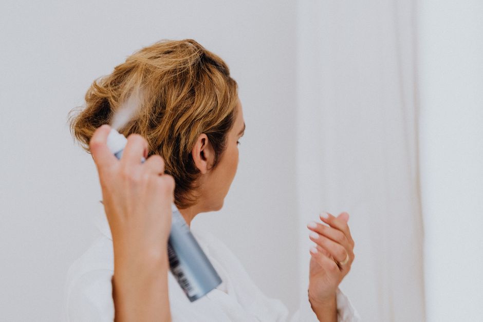 Mulher estilizando cabelo com spray em ambiente interno, destacando cuidados pessoais e beleza feminina.