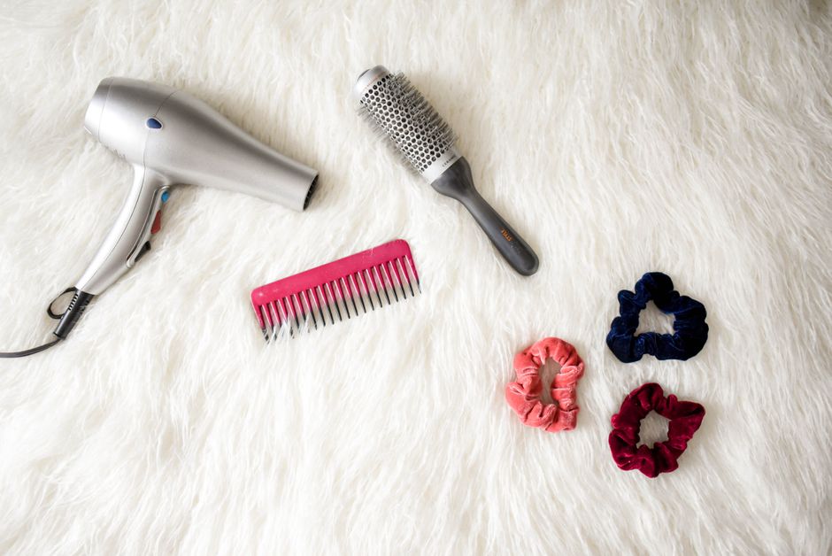 Kit de cuidados para cabelos com secador, escova e elásticos de cabelo dispostos sobre um fundo de pelúcia branca, ideal para dicas de beleza e cuidados capilares.
