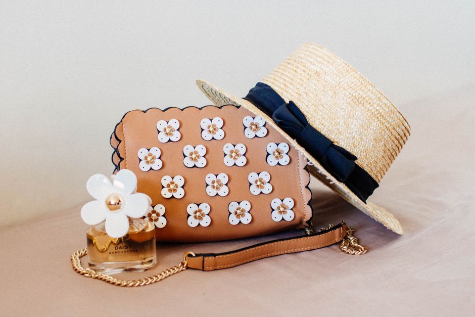 Imagem de itens femininos e acessórios de moda, incluindo bolsa, chapéu de palha, embalagem de perfume e flor decorativa, em um estilo delicado e elegante.