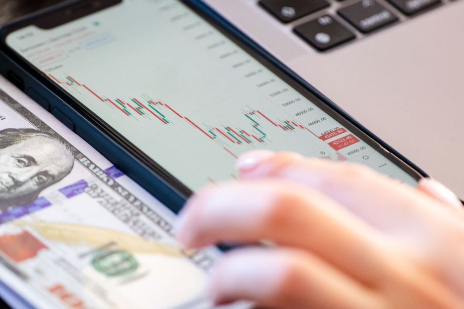 Pessoa monitorando o mercado financeiro em um celular, envolvendo análise de ações ou investimentos;