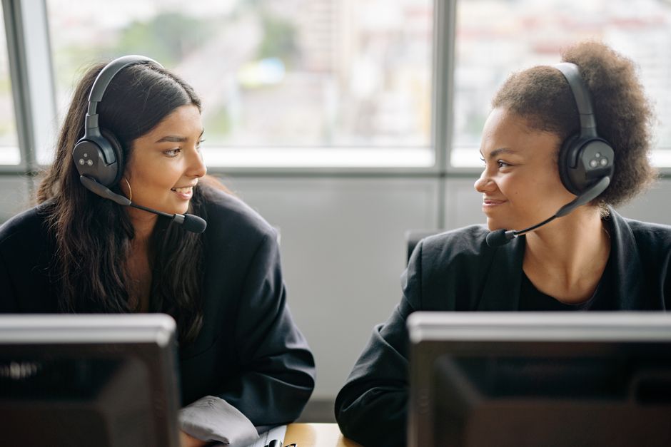 Duas atendentes sorrindo durante atendimento ao cliente, simbolizando suporte e comunicação eficaz em um ambiente de call center ou assistência ao cliente.