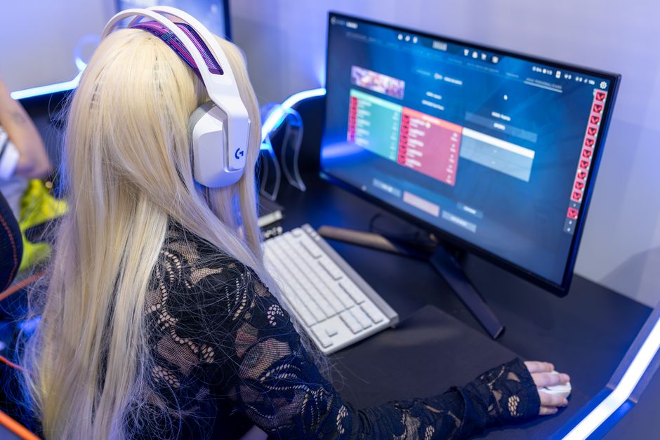 Pessoa jogando videogame em um ambiente com iluminação azul, usando fones de ouvido grandes, em um cenário que remete ao entretenimento digital e cultura pop.