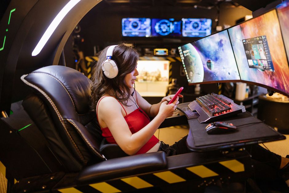 Mulher utilizando um computador de múltiplas telas em um ambiente tecnológico e futurista, possivelmente em um espaço de trabalho inovador ou centro de comando.