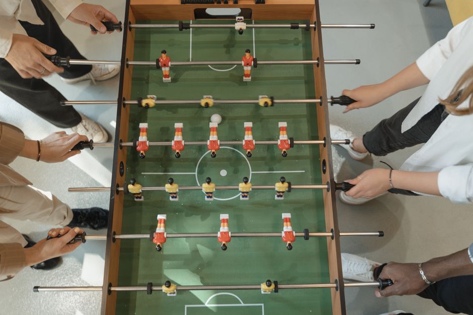 Grupo de pessoas jogando pebolim, simbolizando estratégias colaborativas e trabalho em equipe.