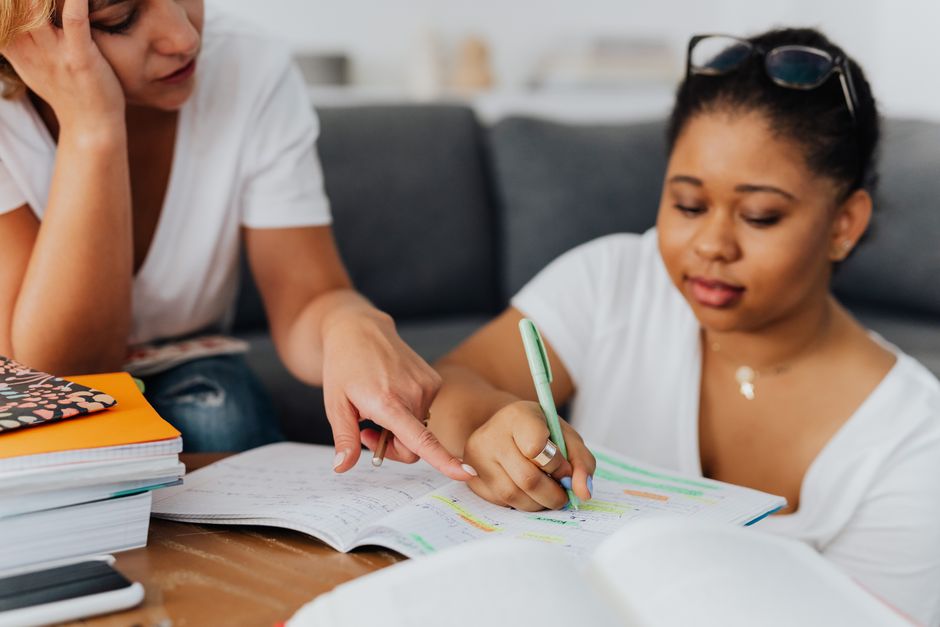 Mulher ajudando uma jovem a estudar, destacando o tema de educação e apoio ao aprendizado.
