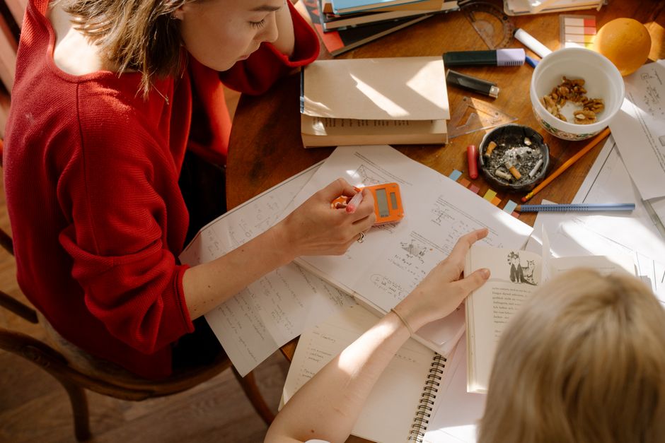 Pessoa estudando com livros e materiais de estudo espalhados sobre uma mesa, em um ambiente de aprendizado ou pesquisa.