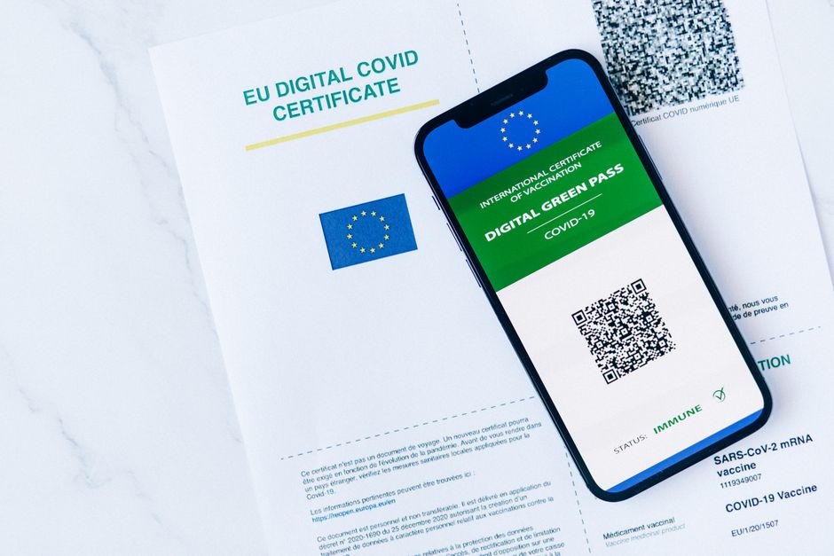 Imagem de um documento de certificado digital de vacinação COVID-19 da União Europeia ao lado de um smartphone exibindo um passaporte de vacinação digital com código QR.