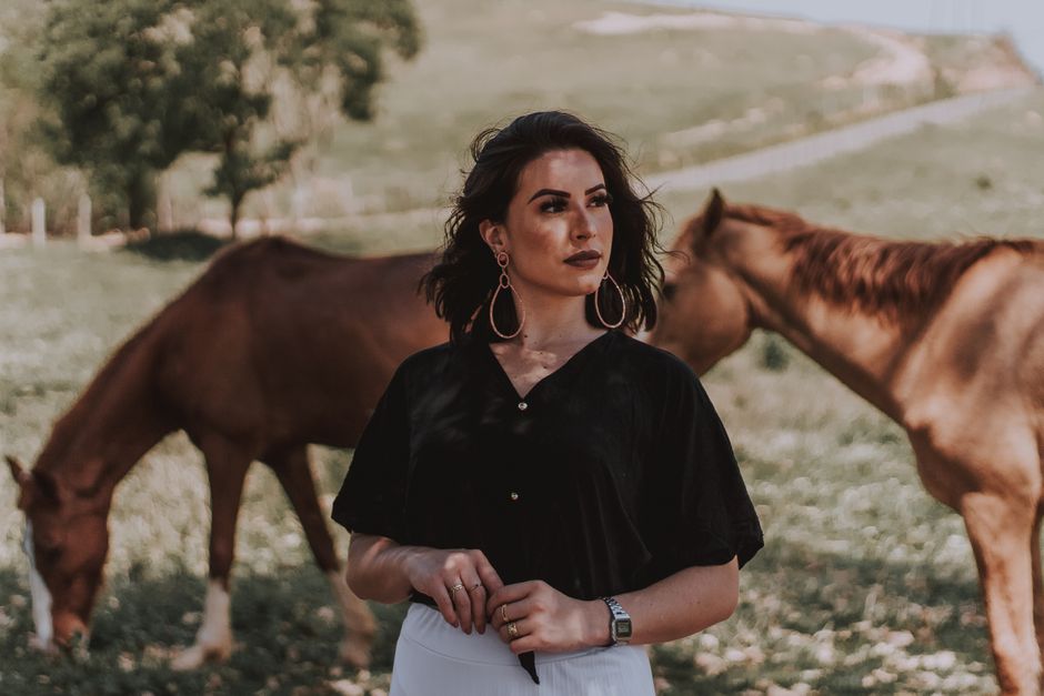 Mulher em um campo com cavalos, refletindo sobre conexão com a natureza e vida ao ar livre.