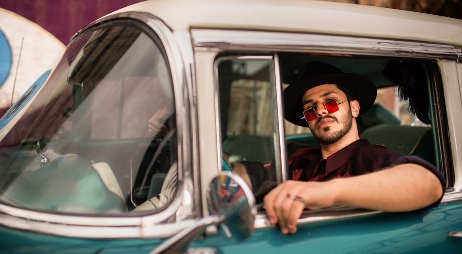 Homem com estilo retrô e roupas sofisticadas posando no carro clássico, transmitindo uma atmosfera de elegância e nostalgia.