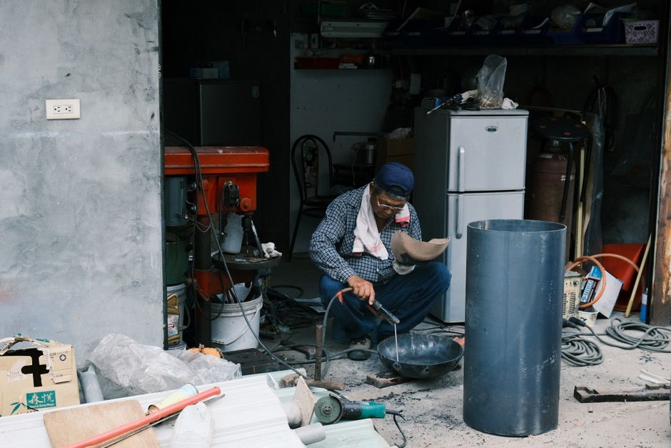 Homem realizando manutenção ou reparo em uma oficina improvisada, destacando aspectos de trabalho manual e ambiente de oficina doméstica ou de pequeno porte.