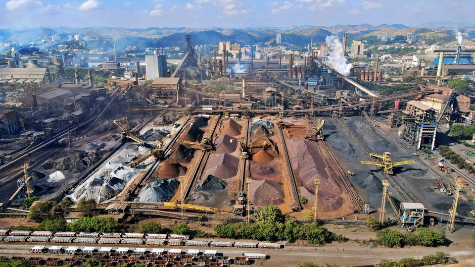 Imagem de uma usina de mineração de carvão industrial com várias pilhas de minério e equipamentos de carga e descarga, representando o setor de mineração e energia.