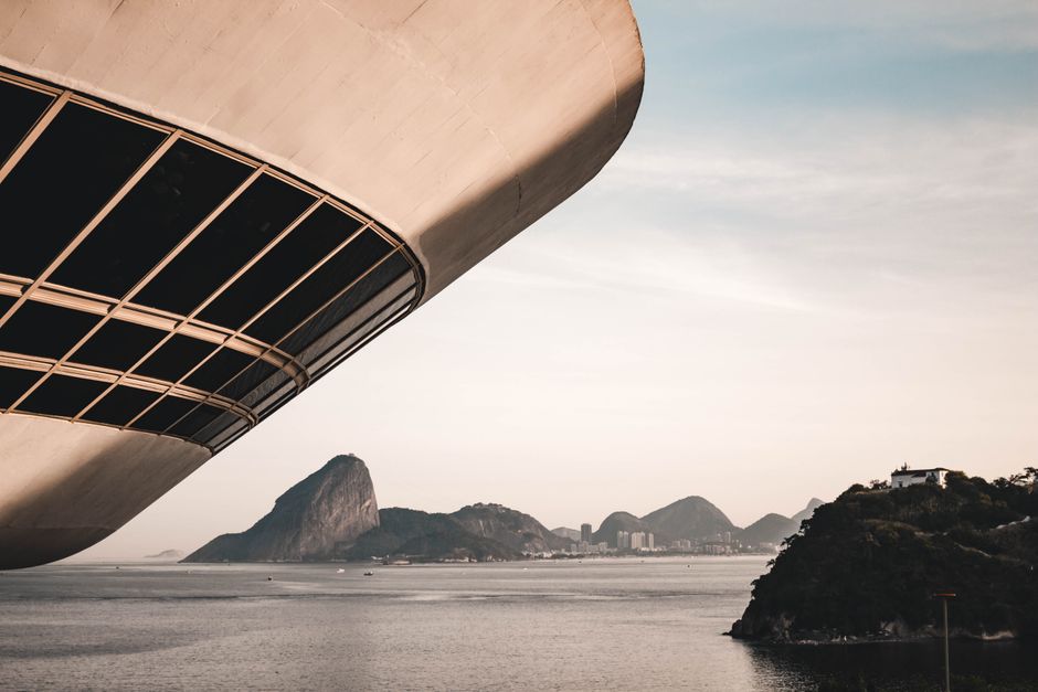 Imagem de uma arquitetura moderna com vista para o mar e montanhas ao fundo, destacando o design inovador de um edifício de construção futurista.