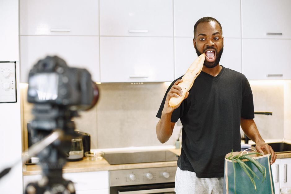 Homem preparando um vídeo divertido enquanto segura um pão na cozinha, ideal para blog sobre criatividade e entretenimento na rotina diária.